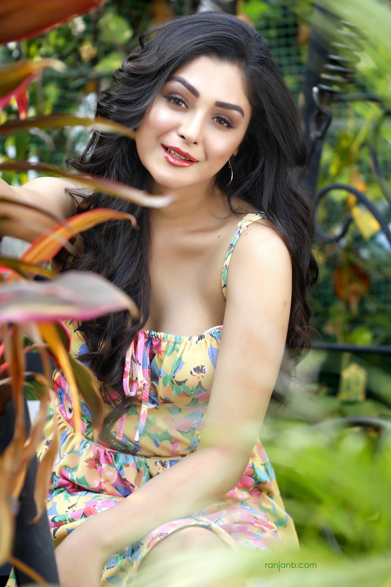 Praniya Paul posing outdoors in a colorful floral dress, surrounded by lush greenery, showcasing a natural light portrait.