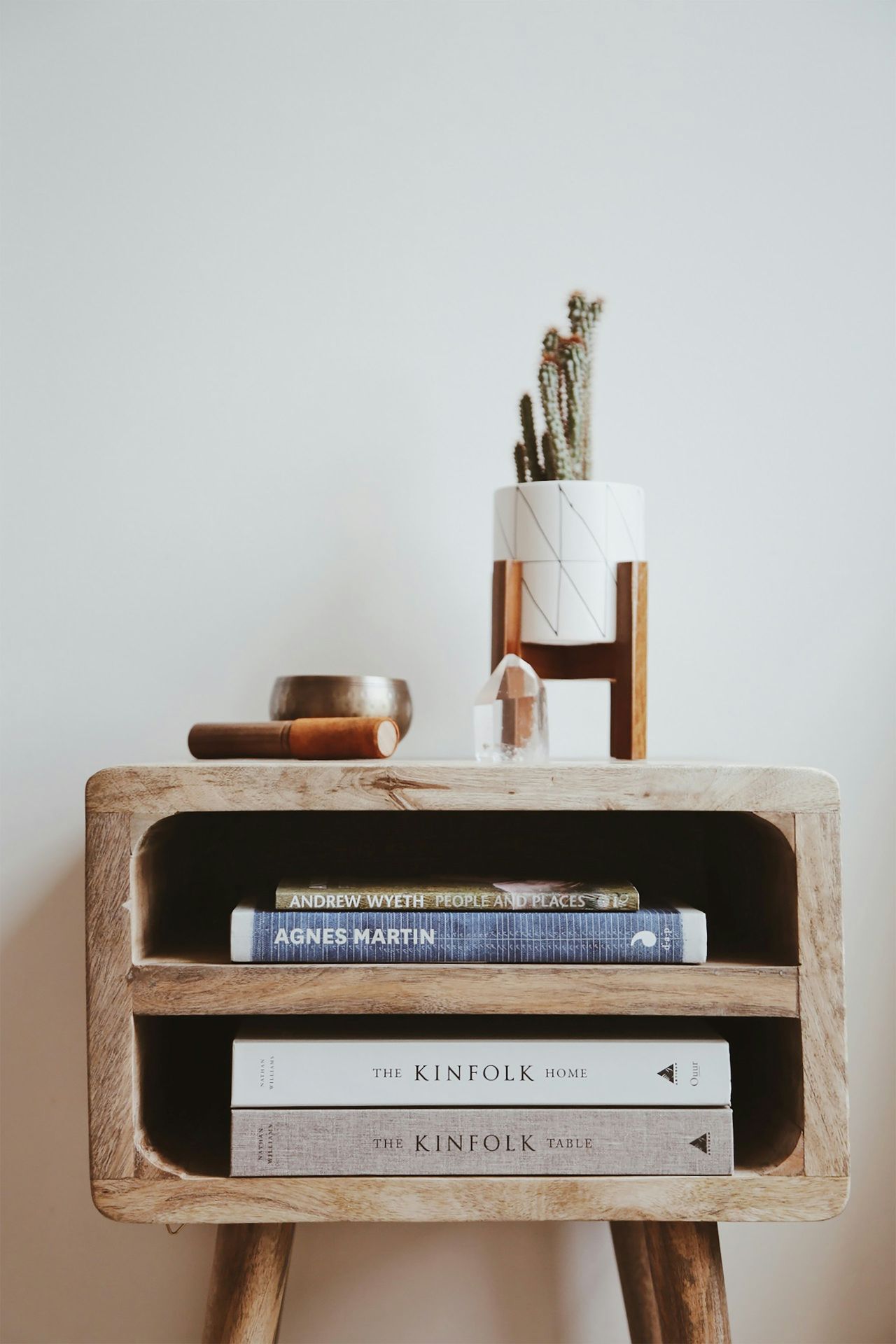 Interior decor featuring a wooden side table beside white wall with books and minimal accessories.