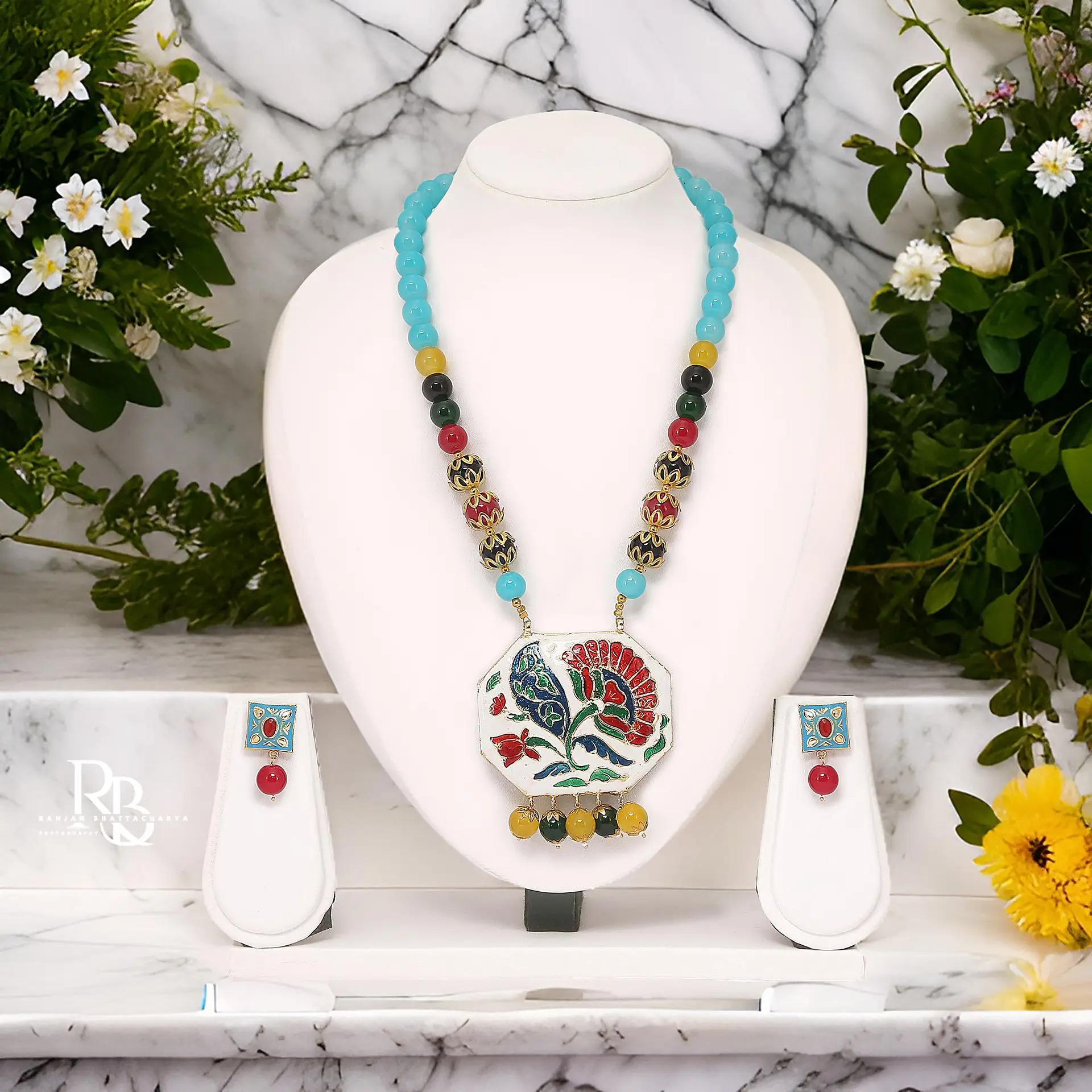 A beautiful necklace with blue and colorful beads and an artistic pendant with floral design displayed on a white mannequin, photographed by the best jewelry photographer in Kolkata, Ranjan Bhattacharya.