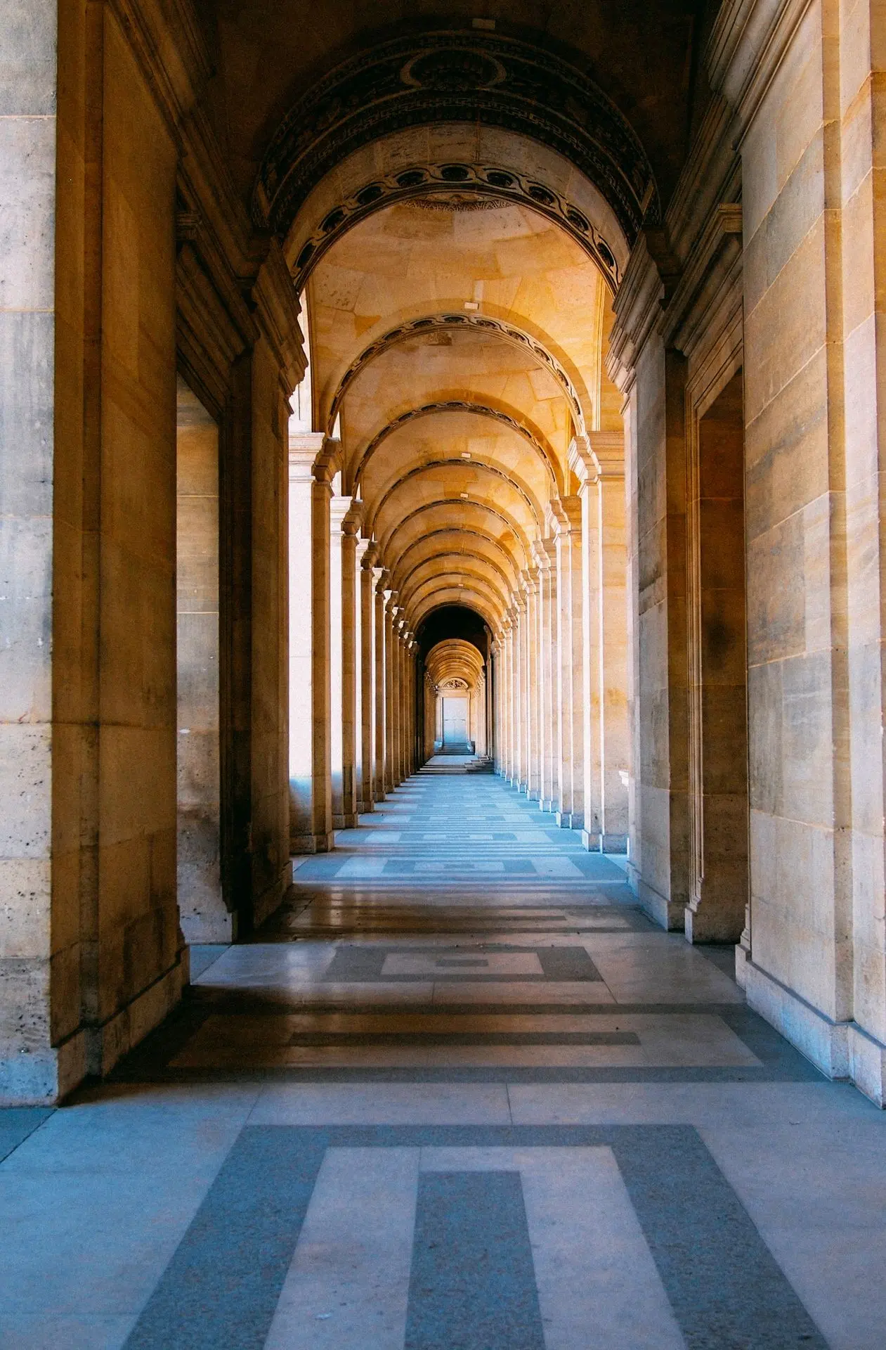 Symmetrical corridor with arches and shadows creating architectural depth.