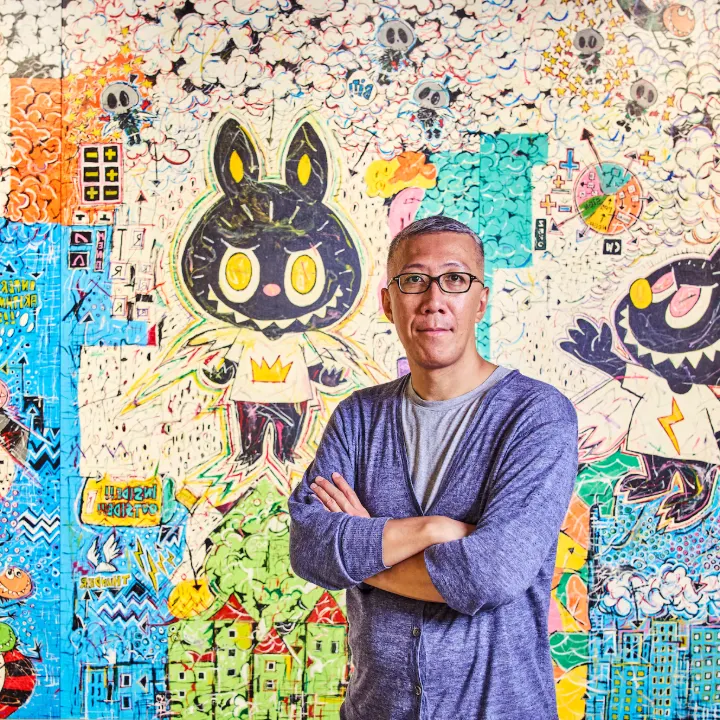 Kasing Lung standing in front of a mural featuring early Labubu characters