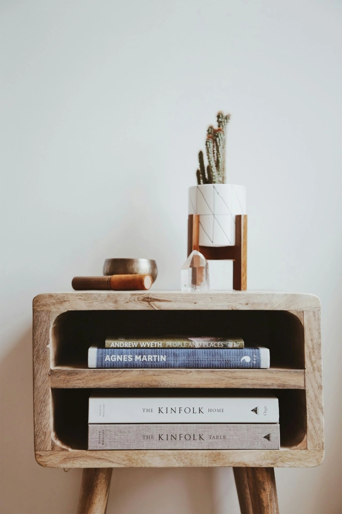 Interior decor featuring a wooden side table beside white wall with books and minimal accessories.