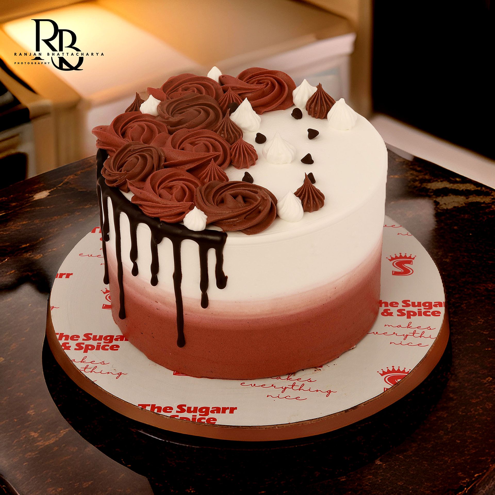 An exquisite cake with vibrant red and white icing and drips, presented in product photography for "The Sugarr and Spice" by Ranjan Bhattacharya.