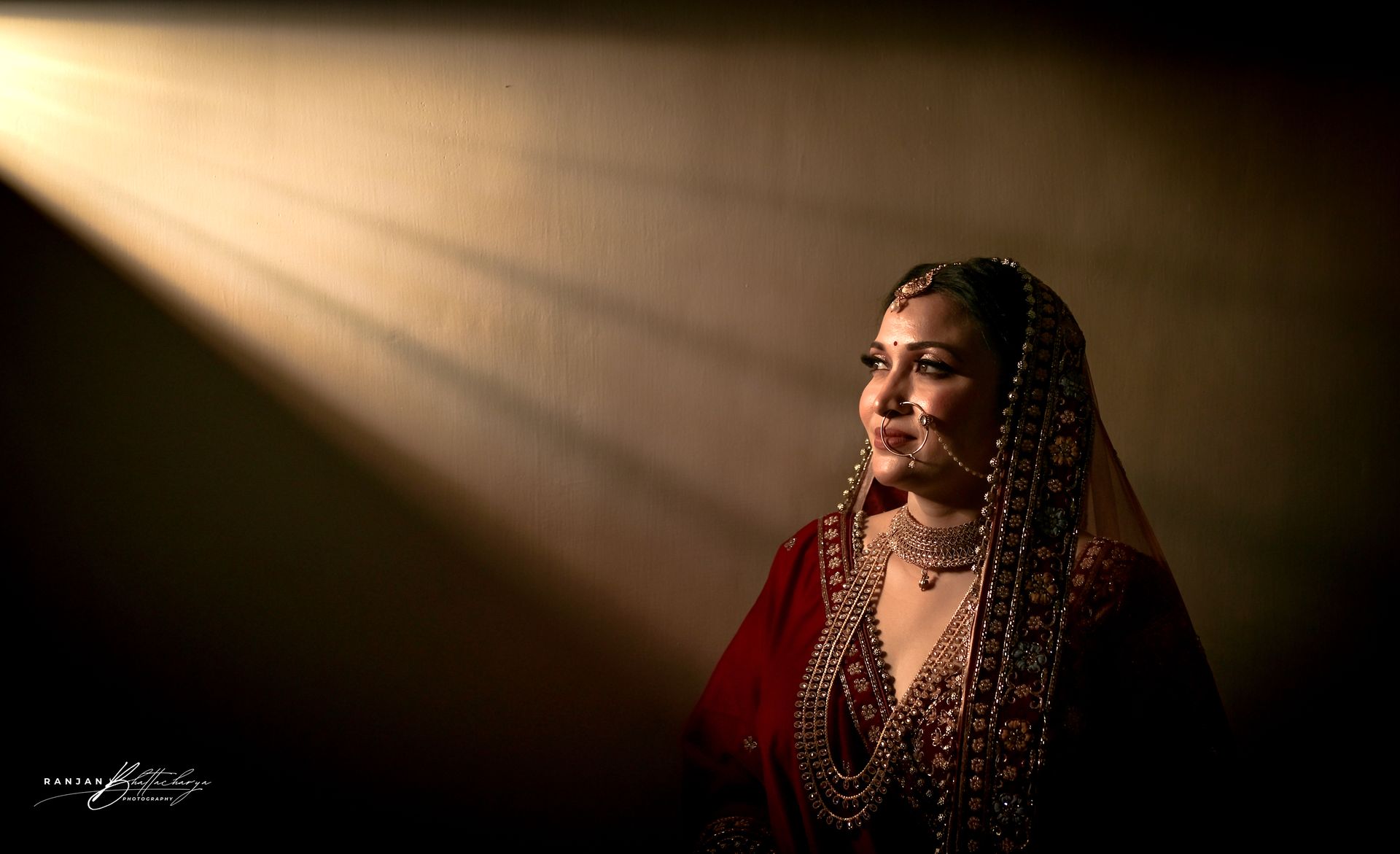 Ruhi Singh, dressed in a rich maroon bridal outfit, illuminated by a soft ring light, ready for her bridal portrait, captured by photographer Ranjan Bhattacharya.