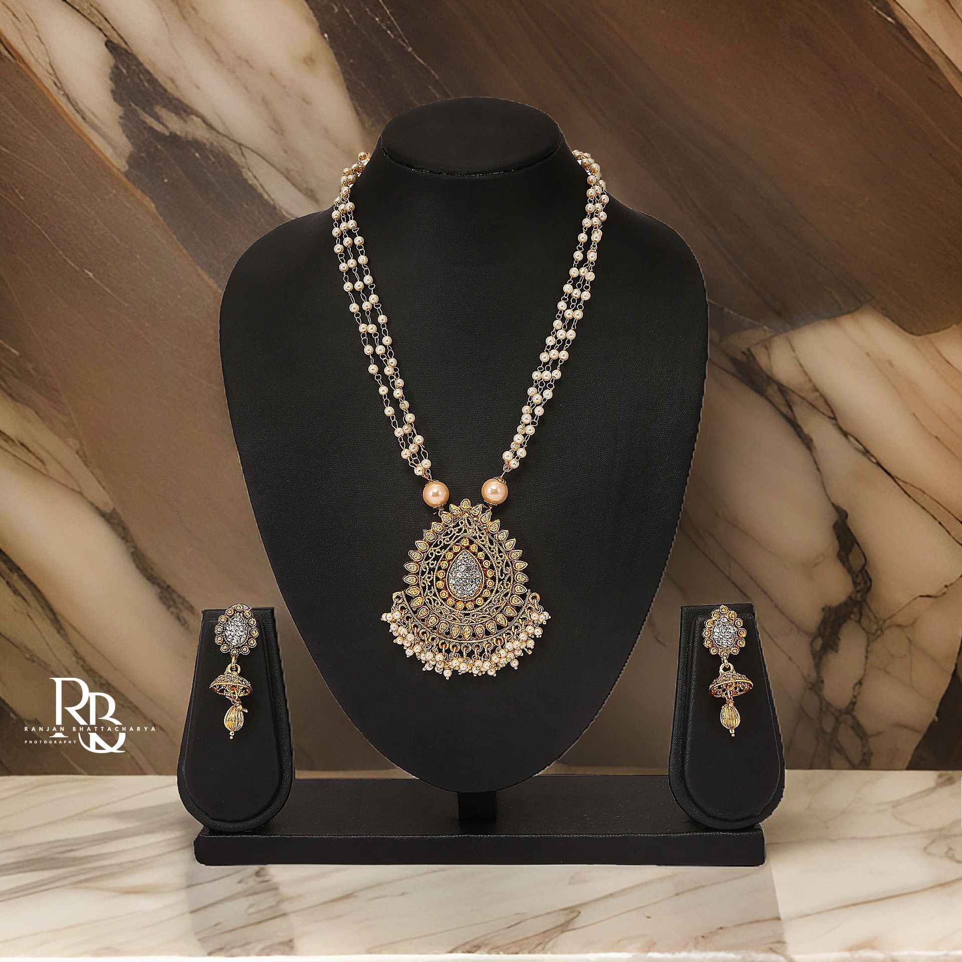 An ornate golden necklace with pearls and gemstones, elegantly displayed on a black mannequin with matching earrings, photographed by Ranjan Bhattacharya Photography.
